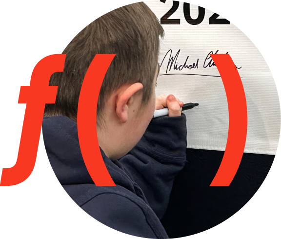 Close-up of a young man’s hand holding a black marker and writing on a white surface, with part of the side of the head visible in the foreground. A large red “f(x)” graphic is overlaid. Small text reads in the bottom left "Caden, Age 19 Living with Duchenne"
